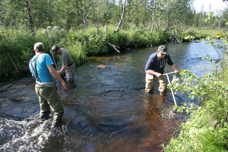 Valokuva, jossa miehet kunnostavat puroa käsityökalulailla.