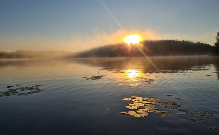 Valokuva, jossa auringonlasku järvimaisemassa.